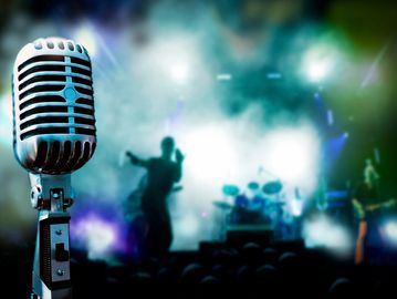A vintage microphone on stage with a blurred band performing in the background.