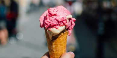 Hand holding a melting strawberry ice cream cone outdoors.