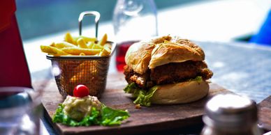 A crispy chicken sandwich with fries and a side dip on a wooden board.