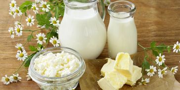 A dairy assortment with milk, butter, and cottage cheese on a wooden table.
