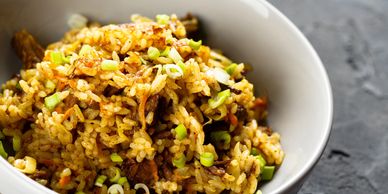 Bowl of flavorful fried rice garnished with chopped green onions.