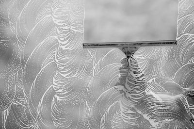 Hand cleaning a glass surface with a squeegee covered in foam.