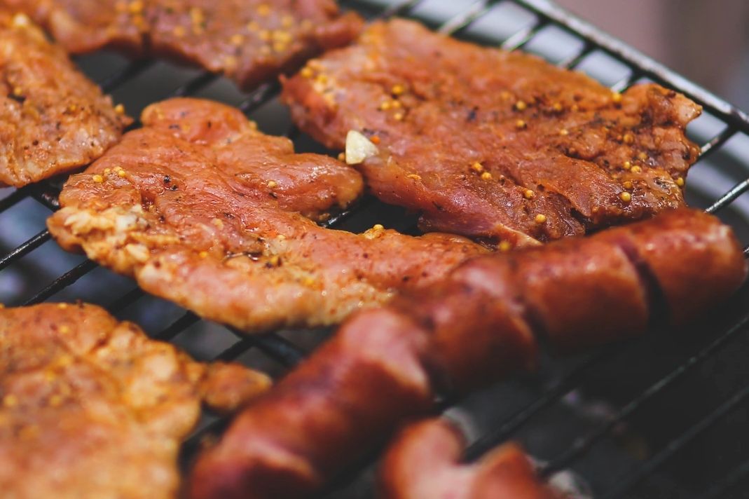 Grilled seasoned meat and sausages cooking on a barbecue grill.