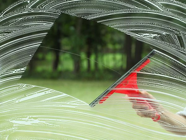Hand using a red squeegee to clean a soapy window.