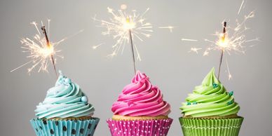 Three multi color birthday party cupcakes with sparklers in each.