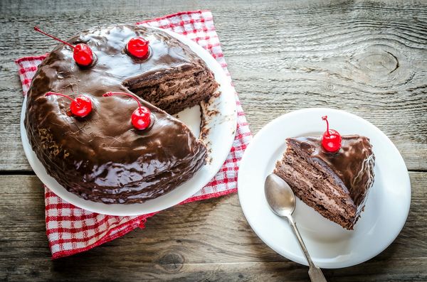 Chocolate cake with cherries on top, one slice served on a separate plate.