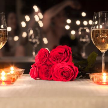 Romantic setting with red roses, candles, and wine glasses on a table.