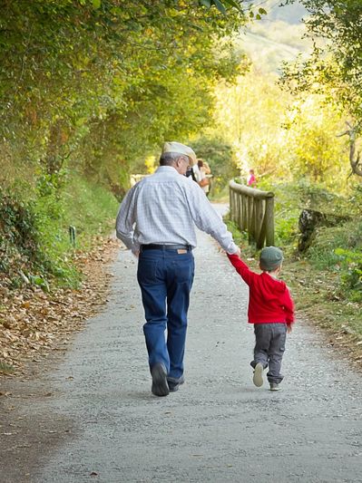 Grandfather and young boy holding hands and walking down a wooded path.