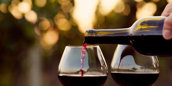 closeup shot of red wine being poured into glasses 