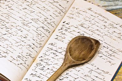 A wooden spoon rests on an open recipe book with handwritten text.