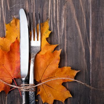 Knife and fork tied with twine on autumn leaves over wooden table.
