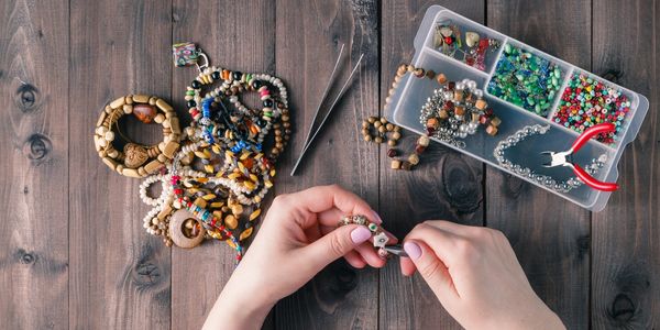 Hands crafting beaded bracelets with colorful beads and tools on a wooden table.