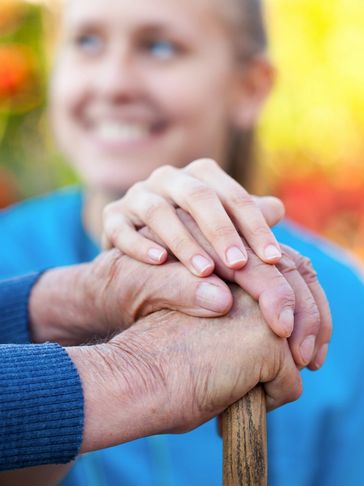 A carer placing her hands on a pair of elderly hands that are holding the to[ of a walking stick