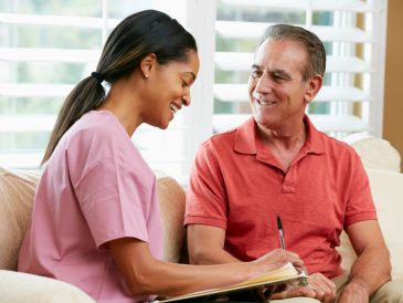 Nurse smiling while taking notes with a senior man.