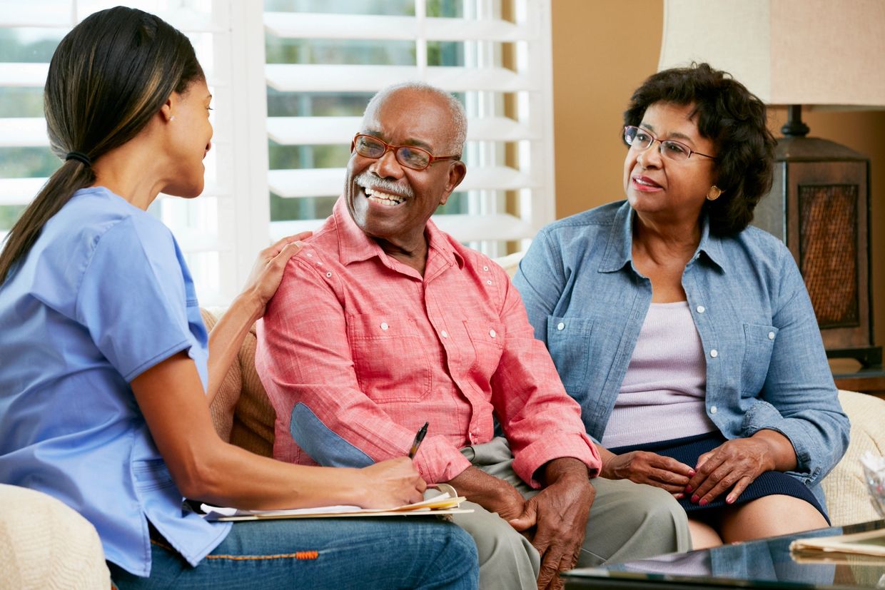 A nurse talking with an elderly couple in a cozy living room.