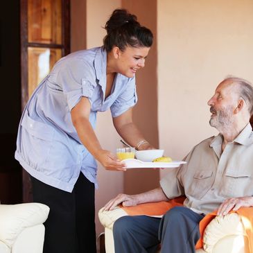 Caregiver serving breakfast to an elderly man in a chair.