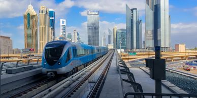 A modern blue train traveling on elevated tracks in a city with skyscrapers.