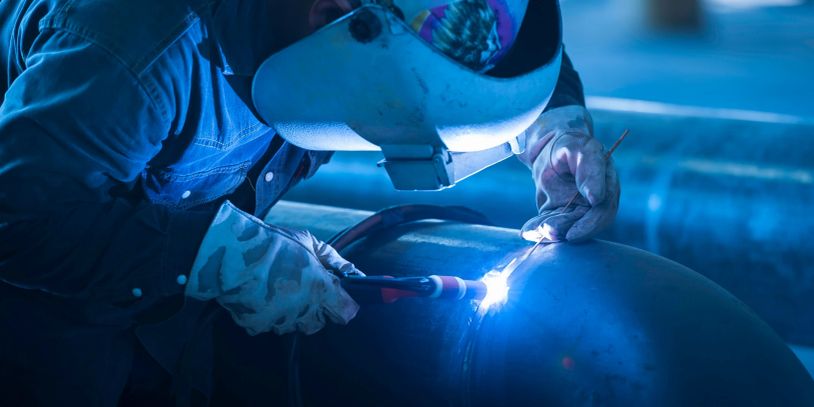 A welder wearing protective gear welding a large metal pipe.