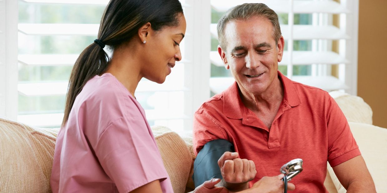 A female caregiver taking blood pressure of a man while they are seated on a couch.