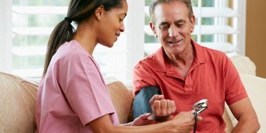 A female nurse sitting next to a gentleman, while taking his blood pressure. 