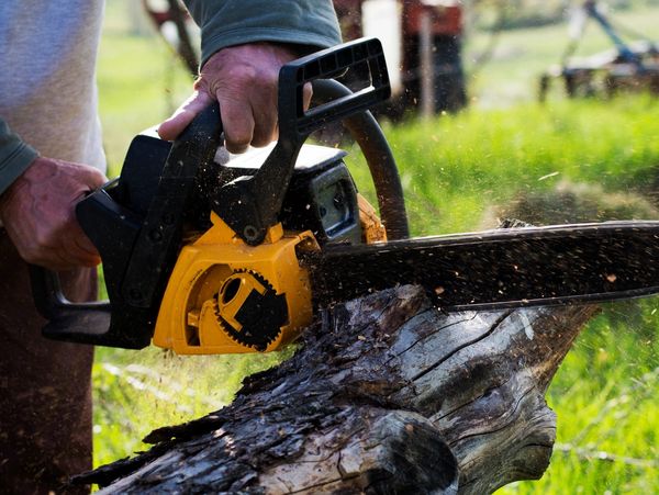 Hands using a chainsaw to cut wood.