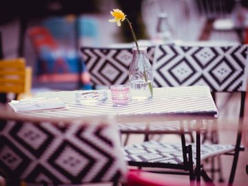A single yellow flower in a glass vase on a patterned table outdoors.