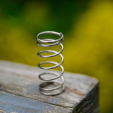 Close-up of a metal spring standing upright on a wooden surface.