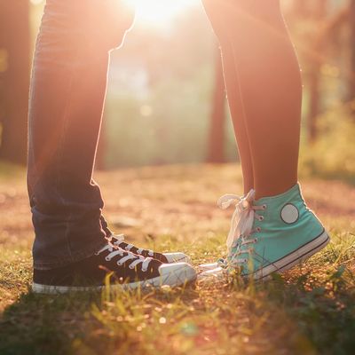 Couple standing close, wearing sneakers at sunset.