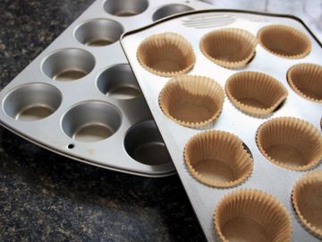 Two muffin pans, one with paper liners, on a kitchen counter.