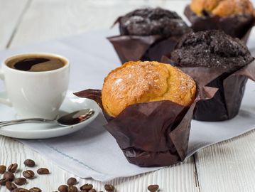 Cup of coffee with assorted muffins on a white table.