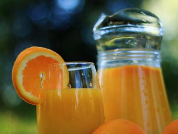 A glass and pitcher filled with fresh orange juice and an orange slice.