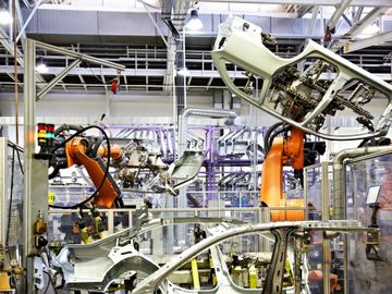Robotic arms assembling car frames inside a modern factory.
