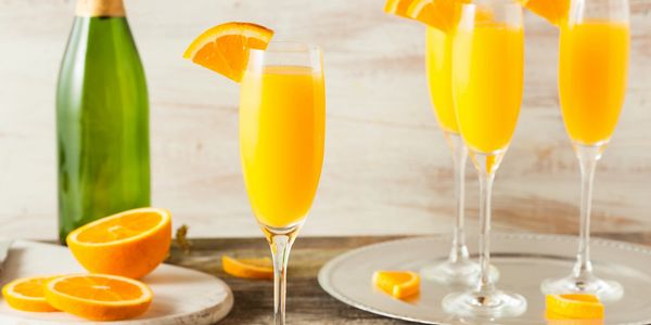 Elegant flutes of orange mimosa cocktails garnished with orange slices, served on a rustic table