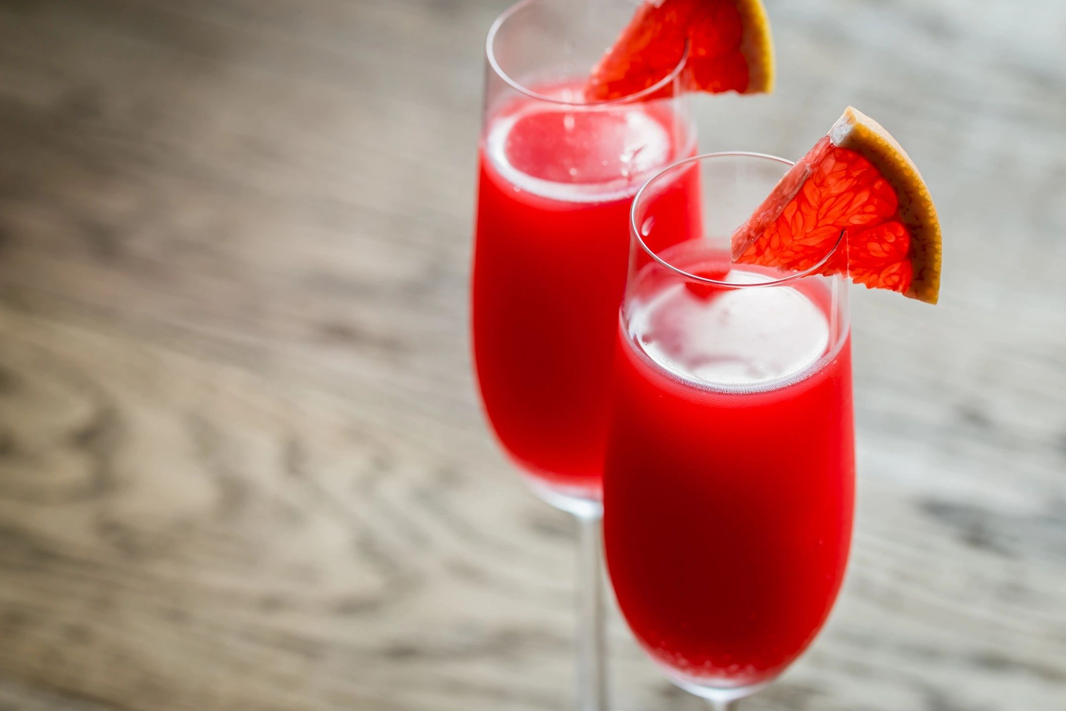 Two champagne glasses with dark red drink and red infused fruit slice garnish