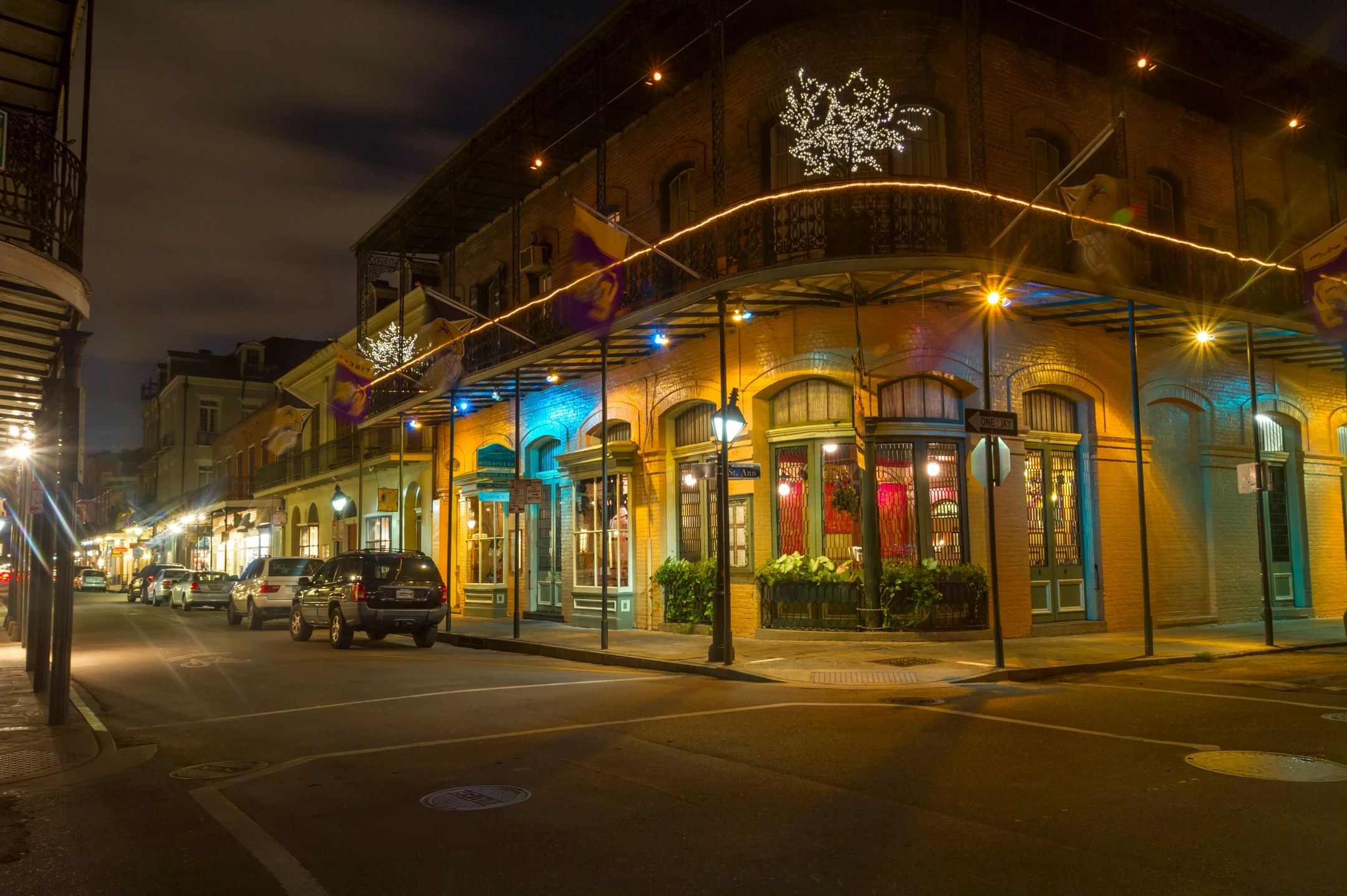A warmly lit street corner with historic buildings and parked cars at night.