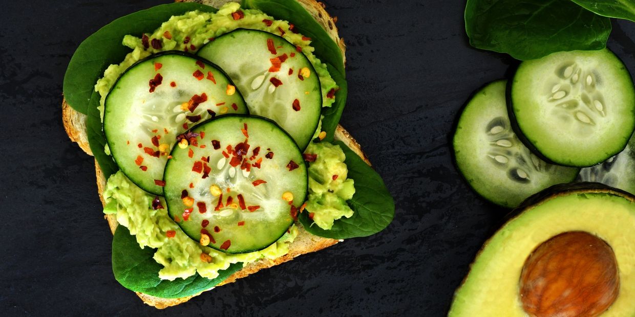 Avocado toast topped with cucumber slices and red pepper flakes on spinach leaves.