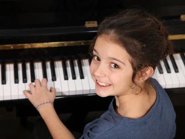 A smiling young girl playing the piano.