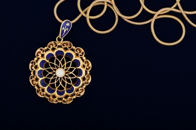 Gold pendant with blue enamel and white center on a chain.