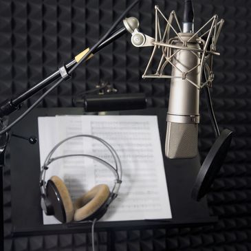 A studio condenser microphone with headphones and voice-over scripts and sheet music on a music stand before a recording session before the jingle singers and voice talent come in.