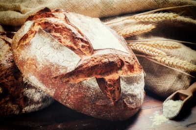 Rustic loaf of bread with wheat stalks and flour on a burlap cloth.
