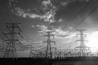 Black and white photo of high-voltage power lines and towers under a cloudy sky.