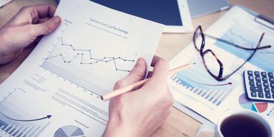 Person analyzing financial charts with a pencil at a desk.