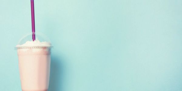 Pink milkshake with whipped cream and a purple straw against a blue background.