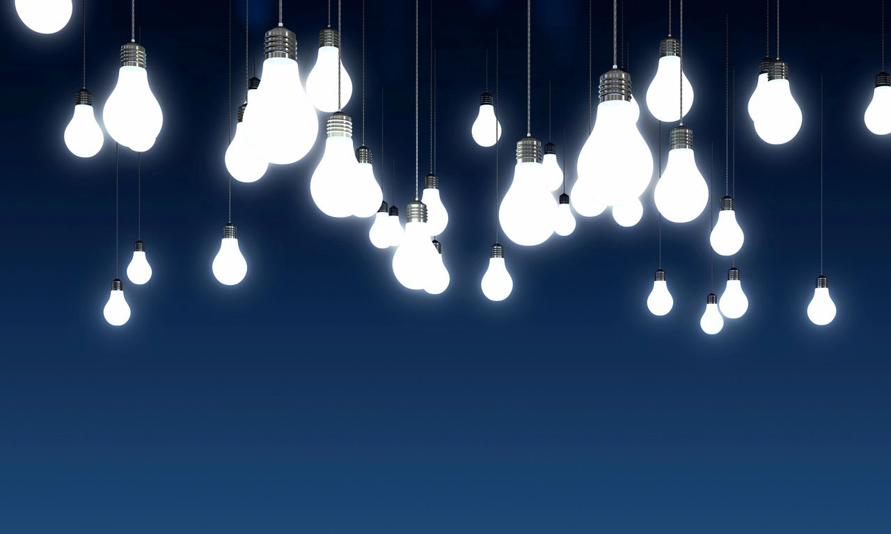 Dark blue back-drop with numerous illuminated light bulbs hanging from their individual cords.