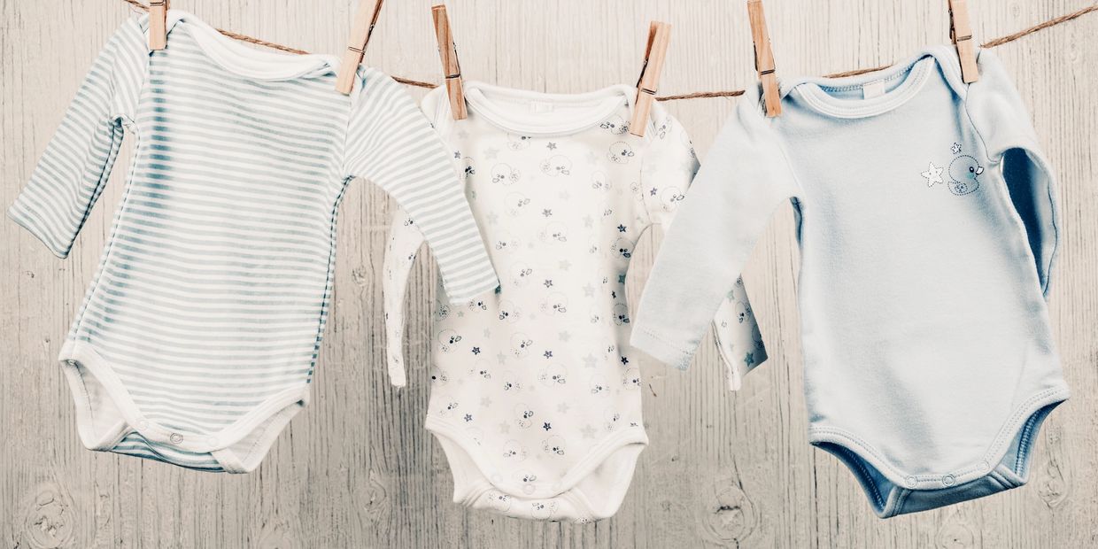 Three baby onesies hanging on a clothesline with clothespins.