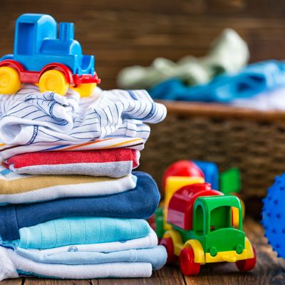 Stack of folded baby clothes with colorful toy trains on a wooden surface.