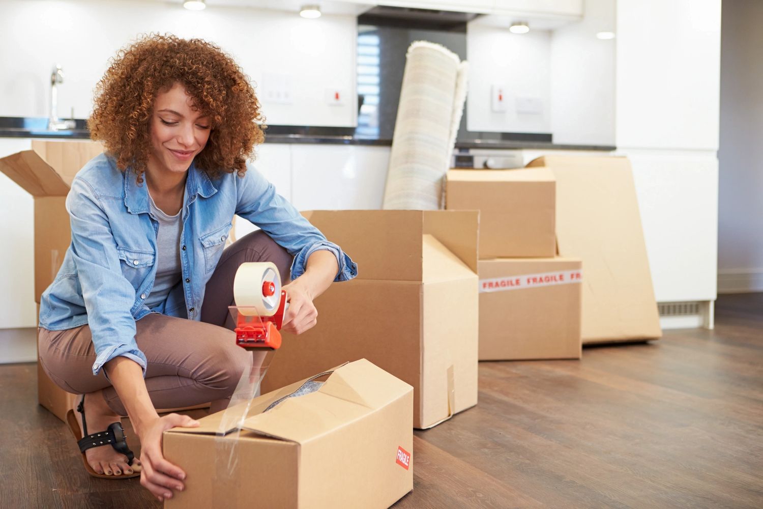 A woman packing boxes with tape in a bright room.