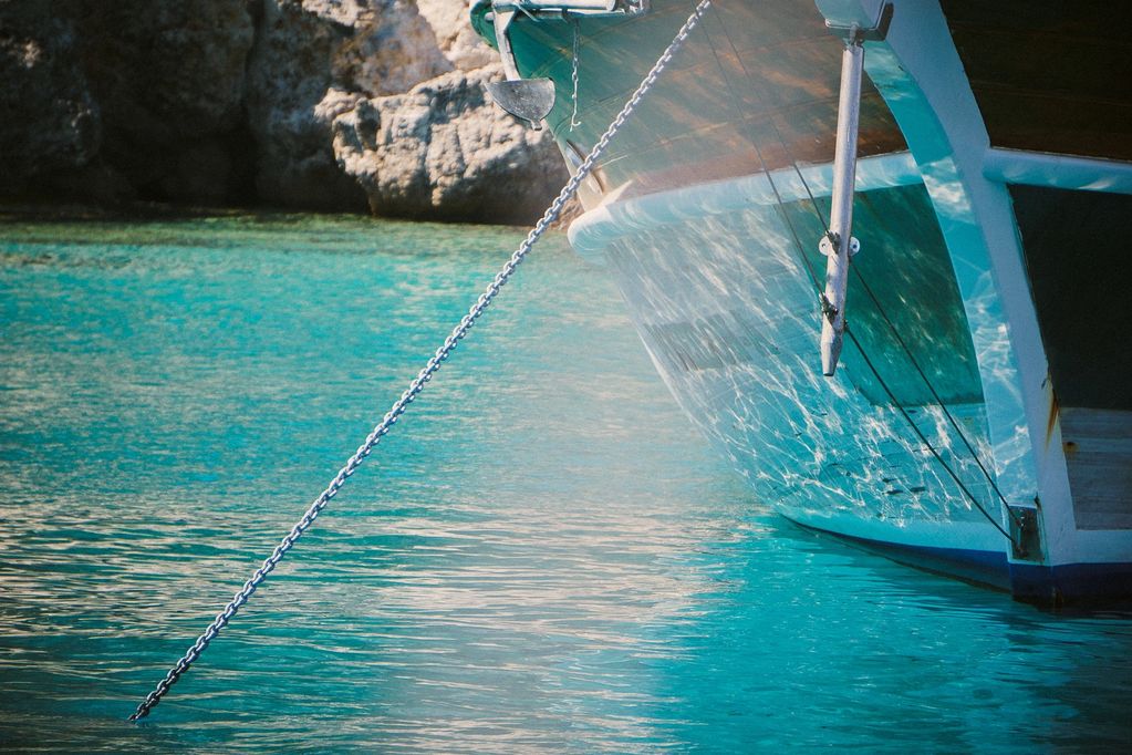 Close-up of a boat anchored in clear turquoise water near rocky shore.
