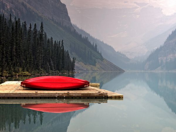 Red canoe on a dock beside a calm mountain lake.