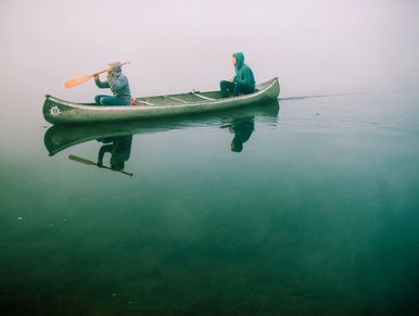 Two people canoeing on calm, foggy water.